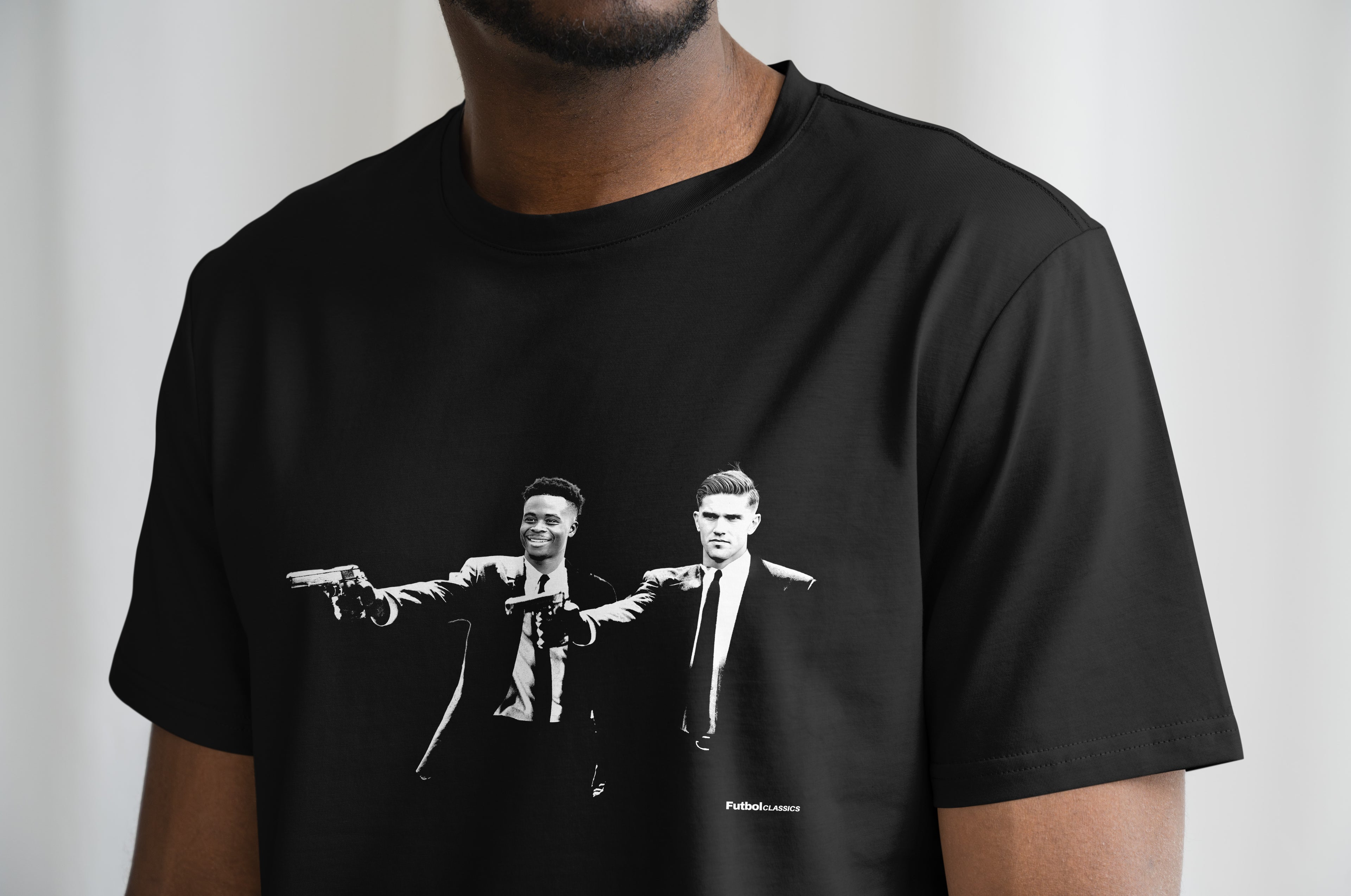 Black t-shirt with graphic design of Aresenal players, Bukayo Saka and Viktor Gyökeres, in the style of pulp fiction. Worn by a person.